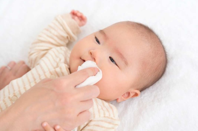 Bunda menggunakan tissue basah untuk membersihkan makanan di mulut bayi